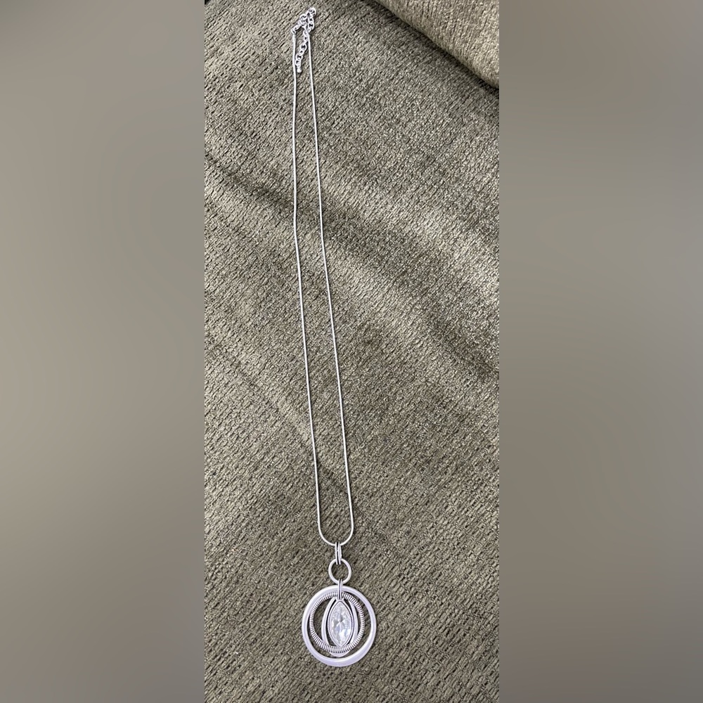 Long silver necklace with multi-loop pendant and clear faceted stone.